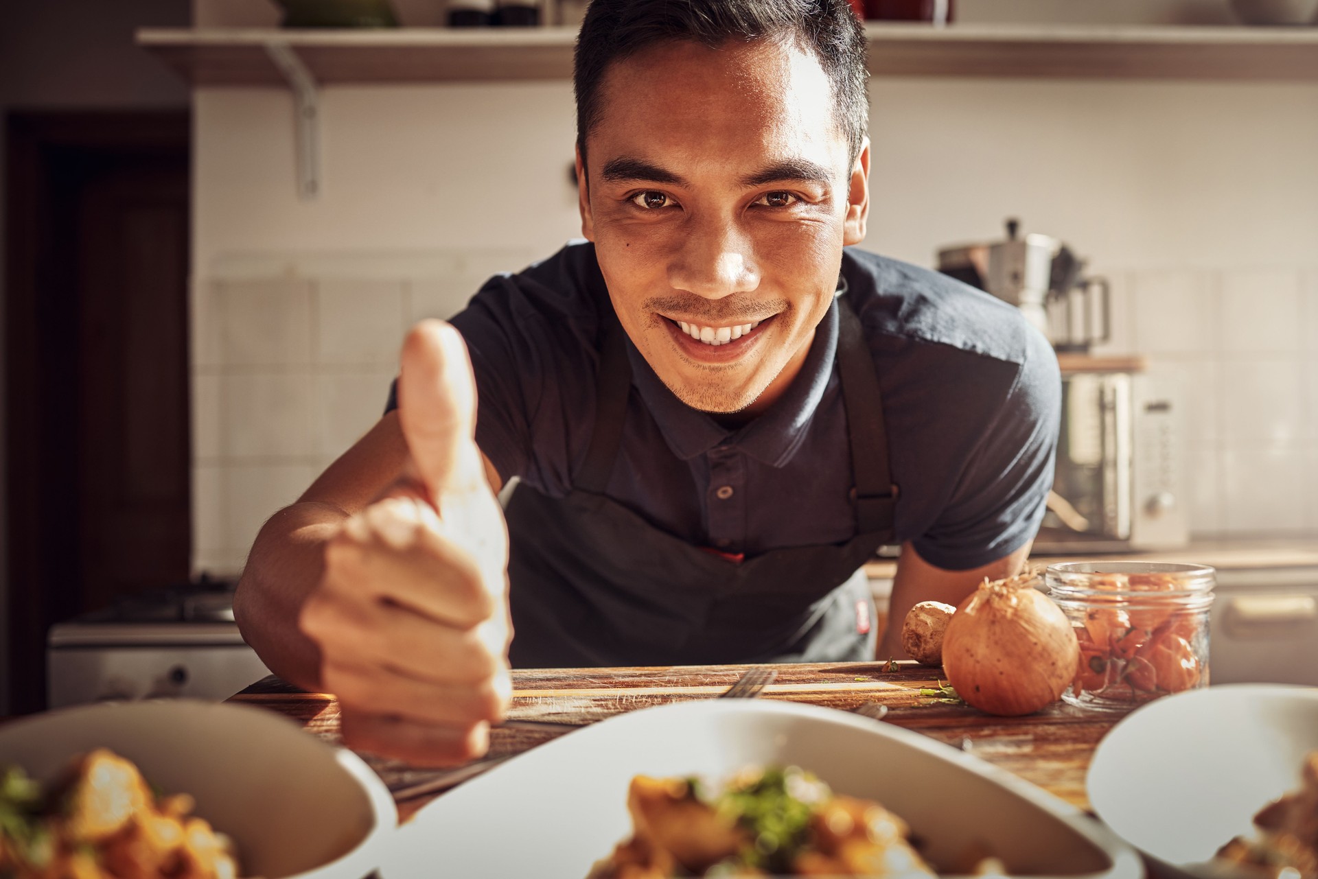 Portrait of a young man showing thumbs up while preparing a delicious meal at home